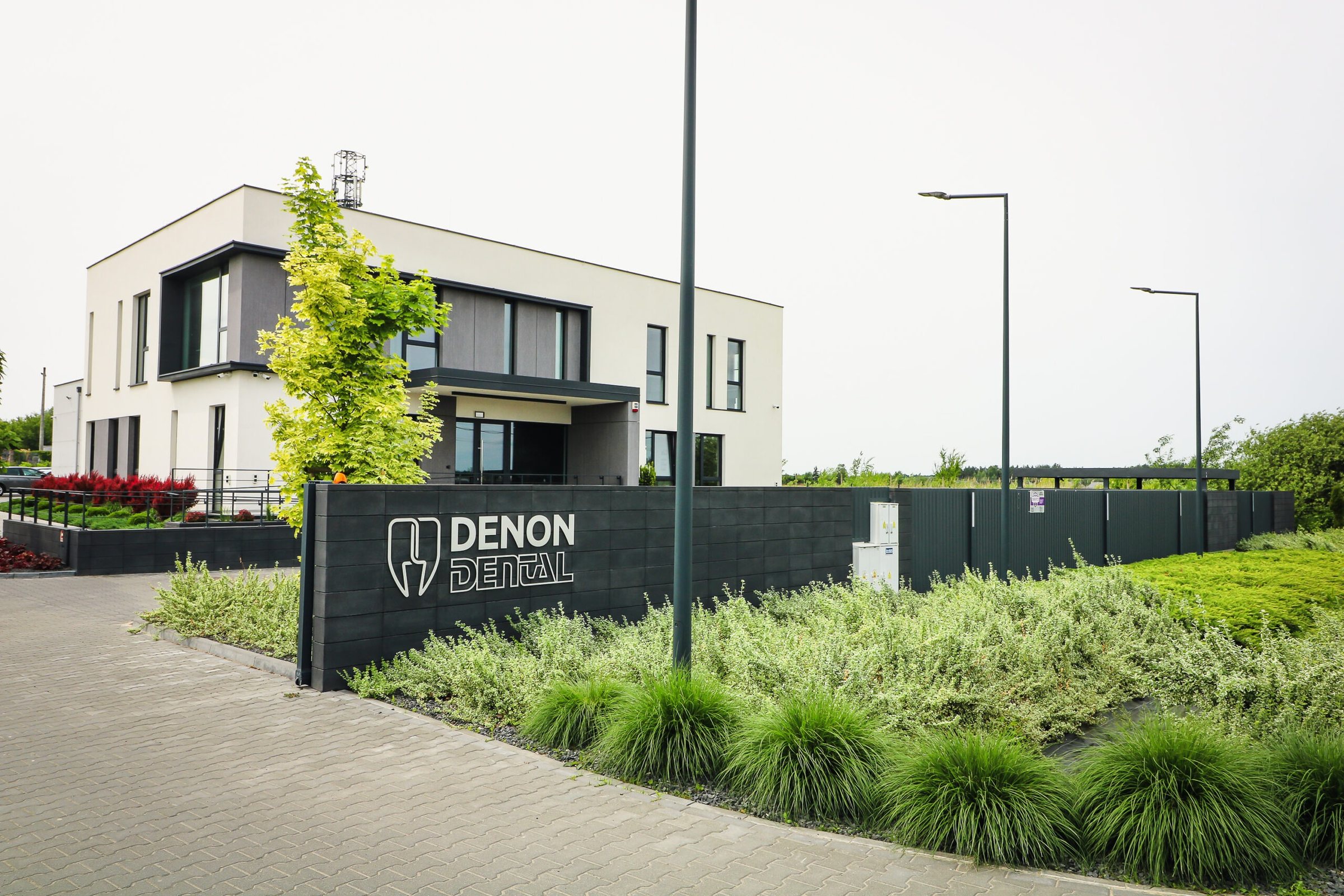 Siedziba Denon Dental w Łubnej pod Warszawą. Grafitowy mur z białym logotypem firmy, za nim budynek biurowy